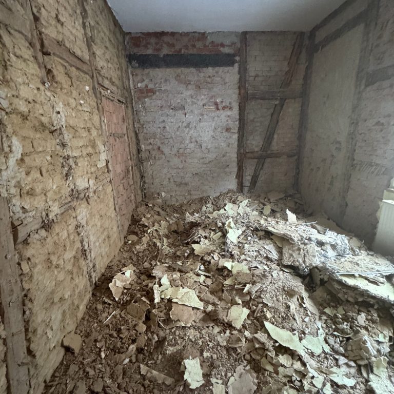 Komplett entkernter Altbau-Raum mit freigelegtem Mauerwerk und Bauschutt auf dem Boden während der Sanierung.