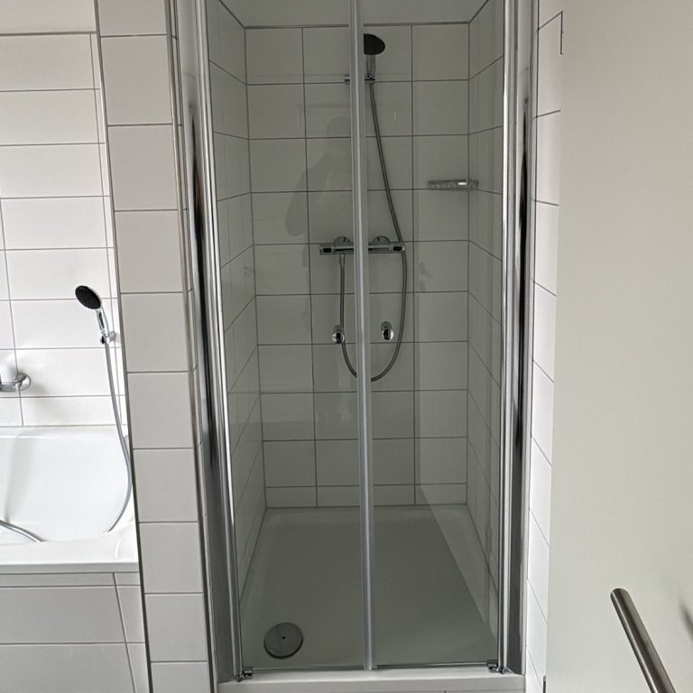 Helles Bad mit Glasdusche und weiß gefliesten Wänden in Bad Harzburg