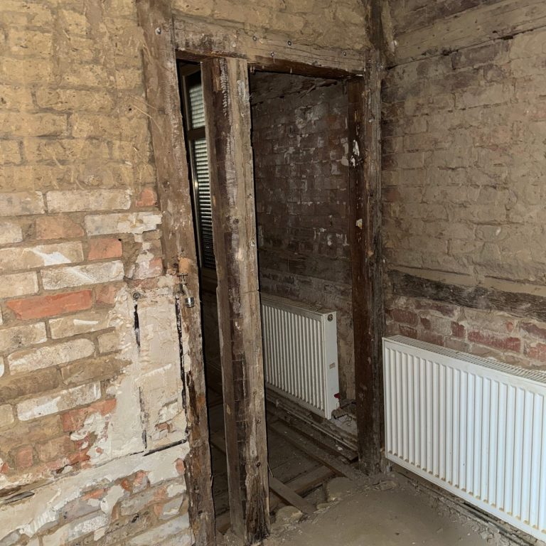 Freigelegter Türdurchgang in entkerntem Altbau mit sichtbarem Mauerwerk und Heizkörpern während der Sanierung.