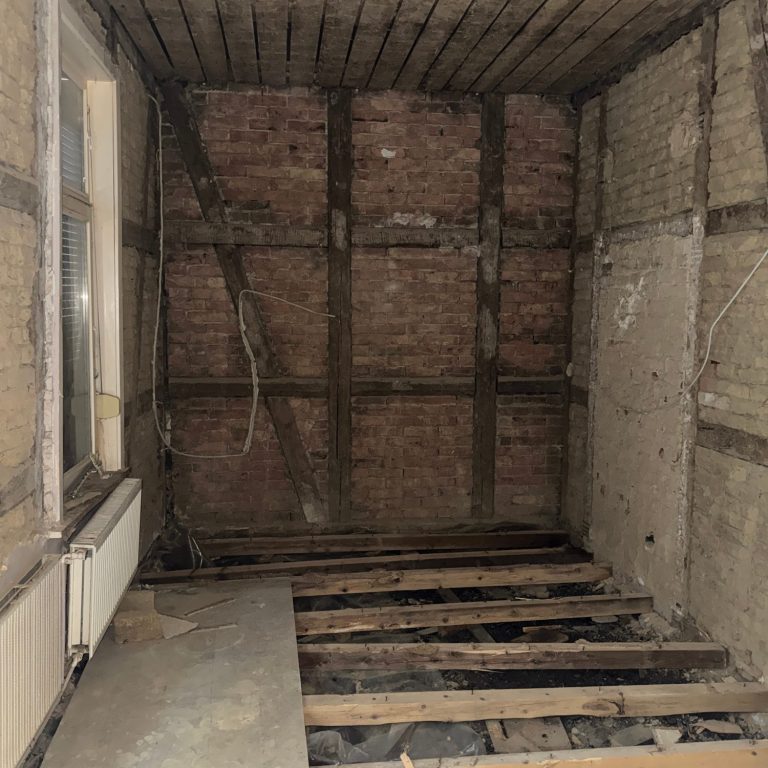 Entkernter Altbau-Raum mit freigelegten Deckenbalken und ausgebautem Boden zur Vorbereitung der Sanierung.